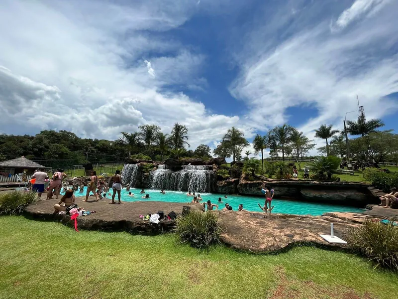 Piscina de cascata cheia de banhistas, com palmeiras e céu azul