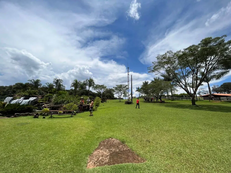 Gramado amplo com árvores e céu de nuvens