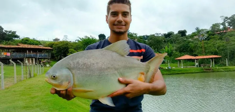 Visitante segurando um tambaqui pescado no lago